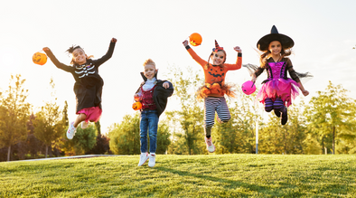 Four children jumping outside and wearing costumes